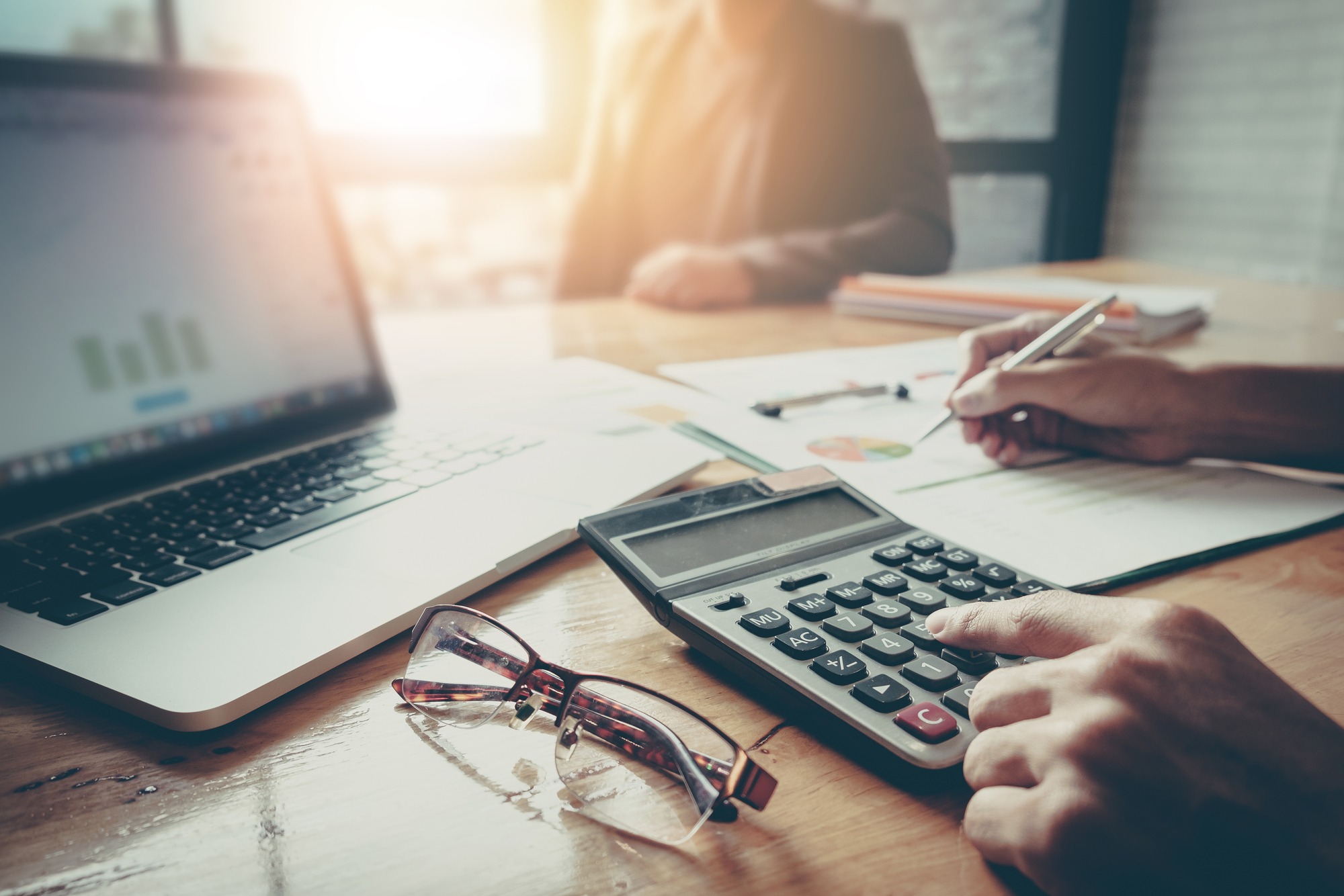 Close up Businessman and partner using calculator and laptop for calaulating finance, tax, accounting, statistics and analytic research concept